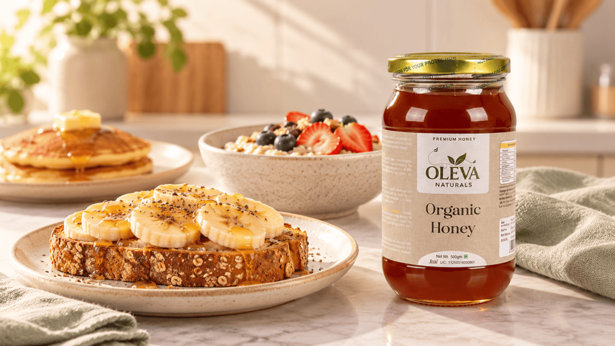 Oleva Naturals Organic Honey jar beside banana toast, a bowl of oats with fruit and pancakes on a breakfast table.
